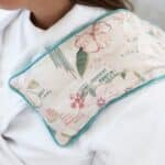 Floral patterned neck pillow with turquoise edging worn around a person's shoulders.