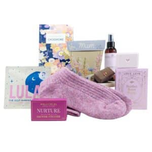 Assorted pamper gift set including a pink knitted sock, chocolates, bath products, and floral packaging boxes for a cozy self-care gift.