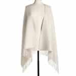 Cream-colored poncho draped over a mannequin with fringe trim along the hem