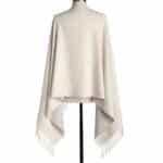 Back view of a cream-colored shawl with fringe trim on the hem, displayed on a dress form