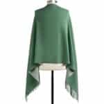 Green poncho or cape on a mannequin, back view with fringe trim along the hem.