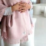 Close-up of a person wearing a pale pink fringed shawl, hands resting over their stomach.
