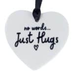 White heart-shaped ornament reading 'no words... Just Hugs' with a small heart, hanging from a black ribbon.