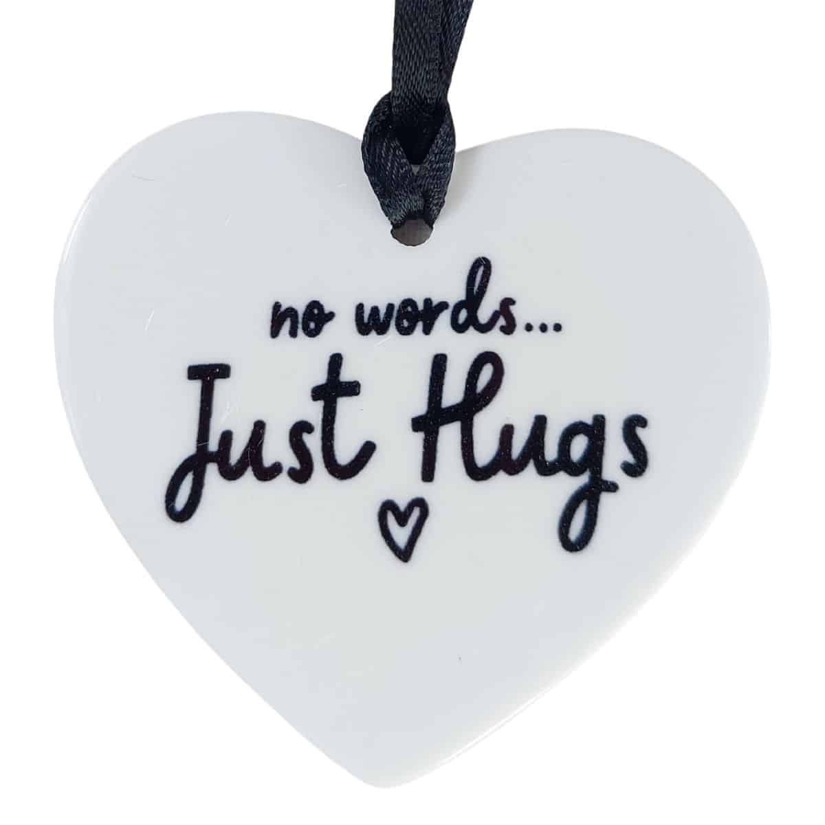 White heart-shaped ornament reading 'no words... Just Hugs' with a small heart, hanging from a black ribbon.