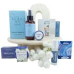 Gift-style collection of bath and beauty products arranged on a round display, including tea, aromatherapy spray, lip balm, vapour rub, and tissues.