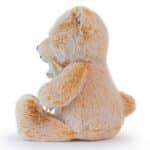 Side view of a light brown plush teddy bear sitting upright with a white satin ribbon bow around its neck, on a white background