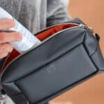 Person places a rolled sheet of paper into a black bag with orange lining, near a silver zipper edge.