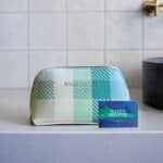 Pastel plaid cosmetic bag with a gold zipper, placed on a counter, with a Sleep & Breathe Shower Steamer box nearby.