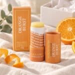 Orange Burst Natural Lip Balm styled with fresh orange slices, neutral linen and an open Sending Hugs self-care gift box