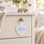 Small Sending Sunshine acrylic heart ornament hanging from a bedside cabinet beside a white gift box in warm natural light.