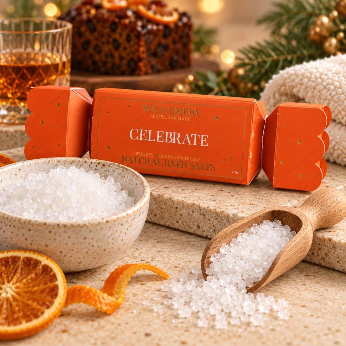 Celebrate Bath Salt Bon Bon with natural white sea salts, wooden scoop and orange slices in a warm Christmas-inspired setting.