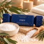 Enjoy Bath Salt Bon Bon with natural white bath salts in a ceramic bowl and wooden scoop, styled in a relaxing neutral bathroom setting.