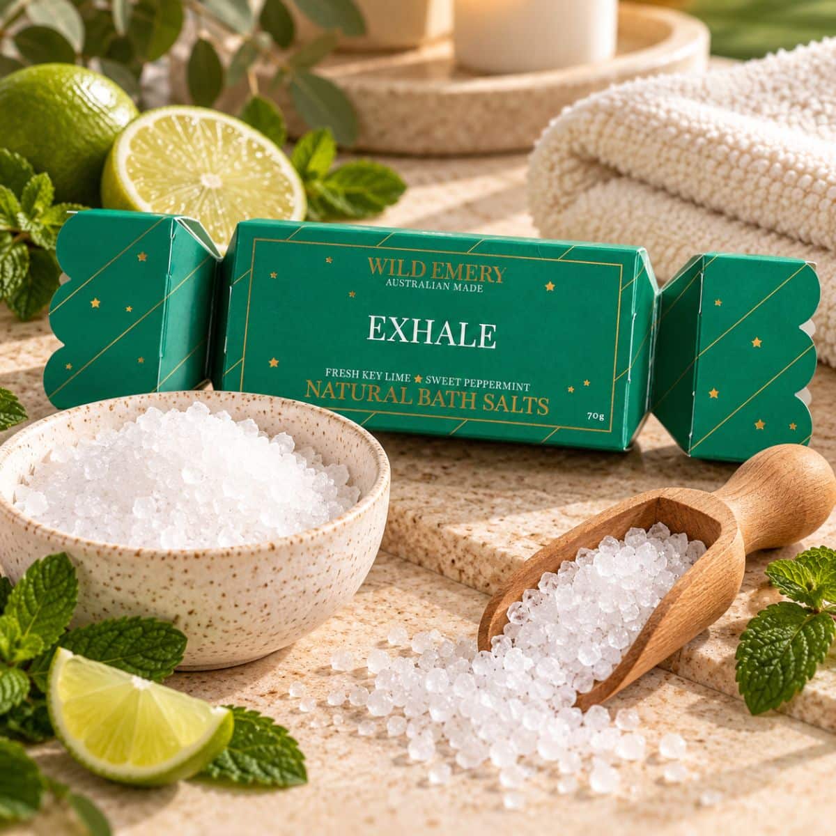 Exhale Bath Salt Bon Bon with natural white Epsom salts, wooden scoop, fresh lime and mint in a relaxing bathroom-inspired setting.